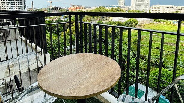 A balcony with a round table and two chairs, overlooking a cityscape with buildings and greenery. - Nature Lovers' Paradise in Iloilo City - Cozy Condo Rental (Iloilo)