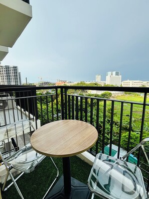 Ein Balkon mit rundem Tisch und zwei Stühlen, mit Blick auf eine Stadtlandschaft aus Gebäuden und Grünflächen.