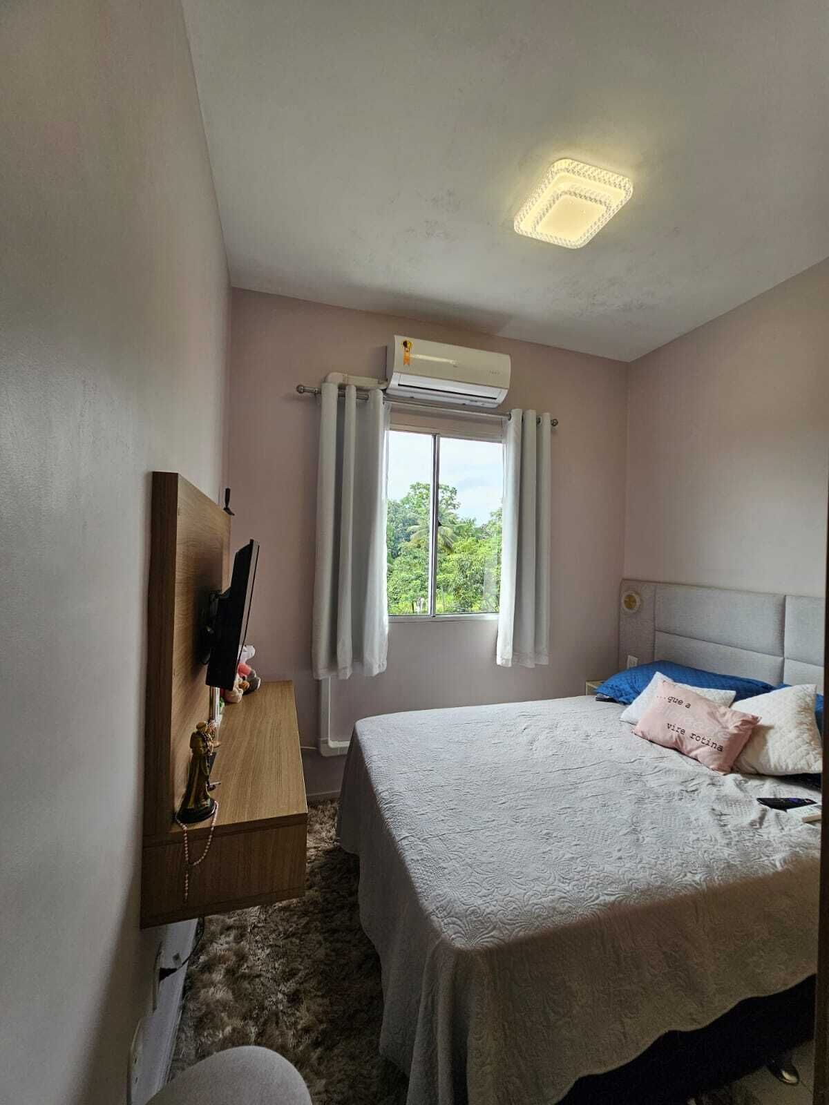 A bedroom with a bed, a TV on a stand, a window with curtains, and an air conditioner.