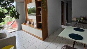 A modern living room with a built-in TV, a dining area with a white table and purple chairs, and a balcony with a hammock. - COP30 Apartment - Total Life Condominium (Tenoné Belém)