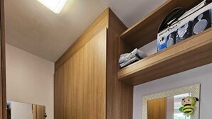 A bathroom with a wooden wardrobe, a vanity with a mirror, and a shelf with toiletries. - COP30 Apartment - Total Life Condominium (Tenoné Belém)