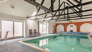 An indoor swimming pool with a clear view of the ceiling structure, a seating area with chairs, and a brick wall with arches. - Pond View Cottage - UK48230 (Tibenham)