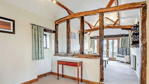 A room with exposed wooden beams, a small wooden table, a radiator, and a view of a balcony with a TV. - Pond View Cottage - UK48230 (Tibenham)