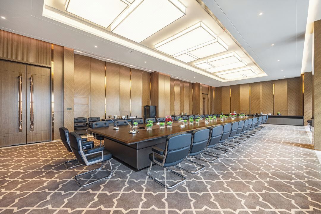 Une salle de conférence dotée d’une longue table, de nombreuses chaises et d’un plafond au design moderne.