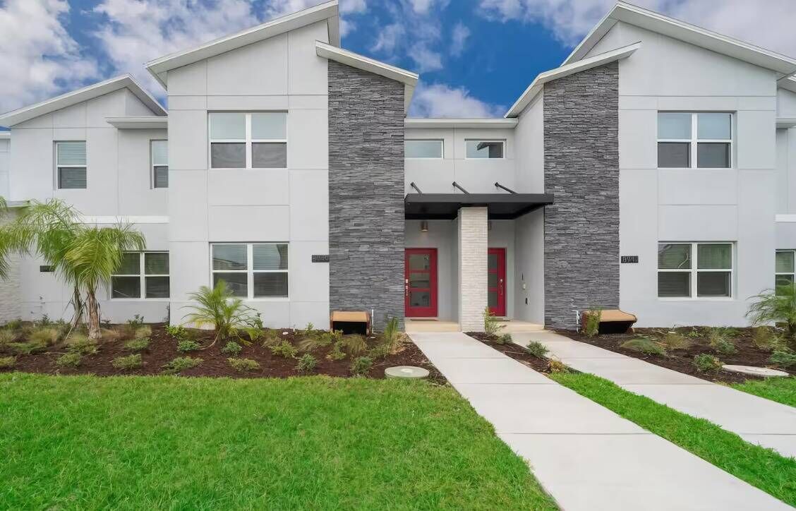 A modern two-story building with a red door, large windows, and a well-maintained lawn.