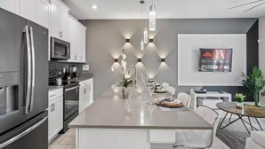 A modern kitchen with stainless steel appliances, a central island with seating, and a flat-screen TV mounted on the wall. - Modern Disney Escape - 4BR - Private Pool (Davenport)