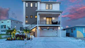 A two-story modern house with a covered driveway, a balcony on the second floor, and a sign indicating it's a vacation rental. - 🏝️ Mod Cottage | 5 BR Home | 2 Minute Walk to the Beach | Private Pool 🌊 (Fort Myers Beach)
