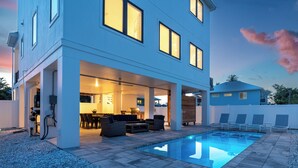 A modern house with an outdoor pool, patio furniture, and a covered dining area. - 🏝️ Mod Cottage | 5 BR Home | 2 Minute Walk to the Beach | Private Pool 🌊 (Fort Myers Beach)