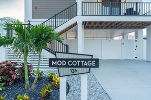 Ein Wohnhaus namens 'Mod Cottage' mit einer Treppe, die zu einem Balkon führt, umgeben von tropischen Pflanzen.