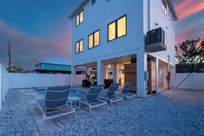Ein modernes, zweistöckiges Haus mit Swimmingpool, Sitzgelegenheiten im Freien und einer überdachten Terrasse.