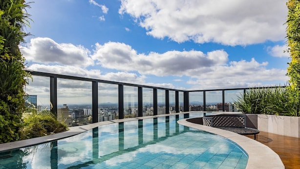 Une piscine à débordement située sur le toit, offrant une vue sur la ville, et entourée de verdure et d’une architecture moderne.