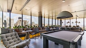 Un espace de détente moderne doté d’une table de billard, de sièges confortables et de grandes fenêtres offrant une vue sur la ville.