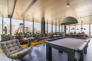 A modern lounge area with a pool table, seating, and large windows offering city views. - Carlos Gomes Square by My Way (Porto Alegre)