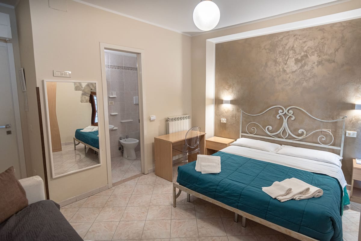 A hotel room with a bed, bedside table, mirror, and a view of the bathroom.