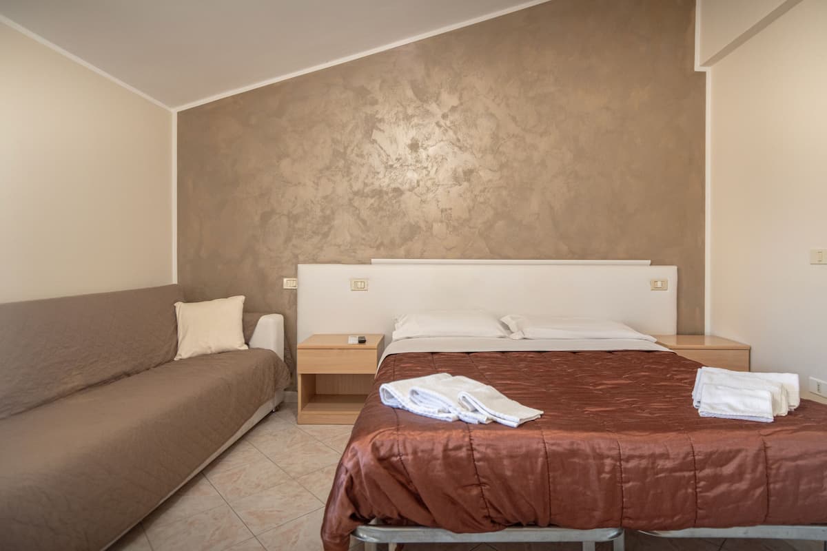 A hotel room with a bed, a sofa, a nightstand, and a wall with a textured finish.