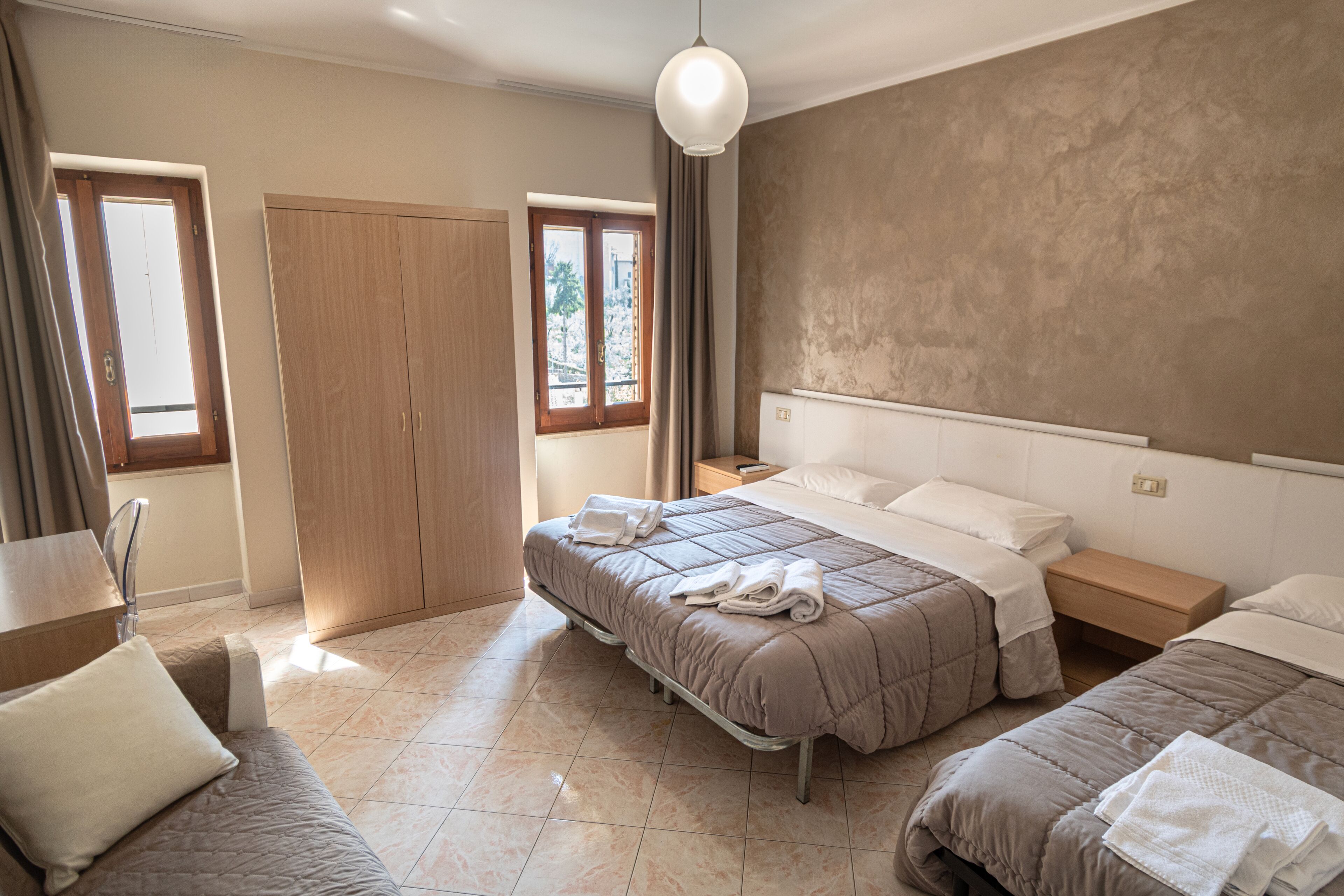 Une chambre d’hôtel avec un grand lit, un lit plus petit, une armoire, une table de chevet et un luminaire suspendu.