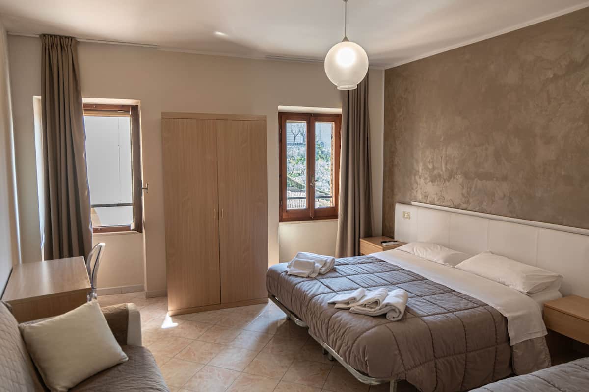 A hotel room with a bed, a sofa, a desk, a wardrobe, and a window with curtains.