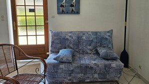 Uma sala de estar com um sofá coberto em tecido jeans, uma porta de madeira e um quadro de veleiros na parede.