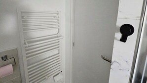 Uma casa de banho com porta branca, porta-toalhas e sanita.