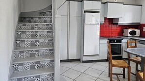 Cozinha com escada e azulejos estampados, armários brancos, backsplash com ladrilhos vermelhos e micro-ondas.