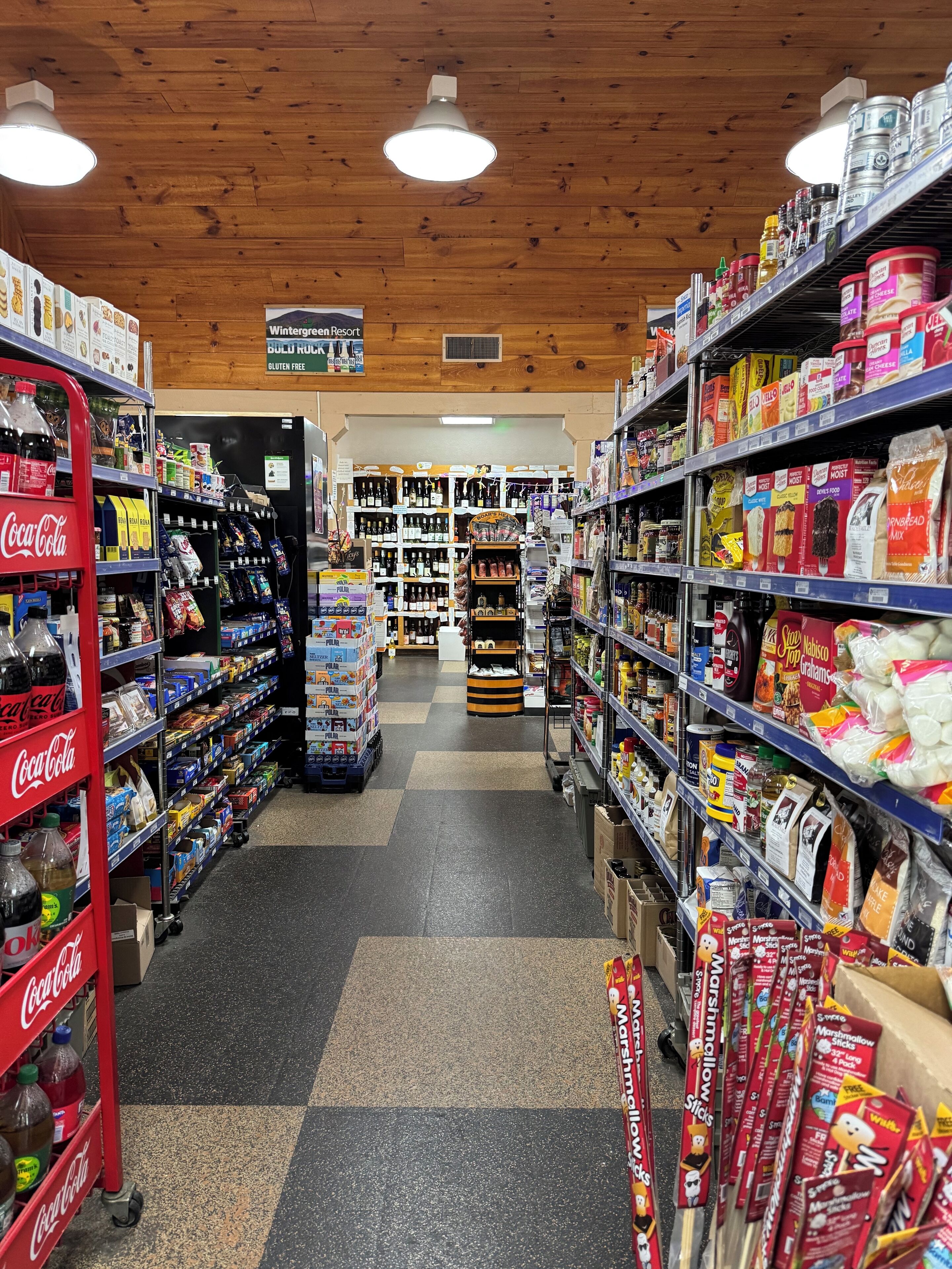 Een gang in een supermarkt met schappen vol diverse producten, waaronder snacks, dranken en huishoudelijke artikelen.