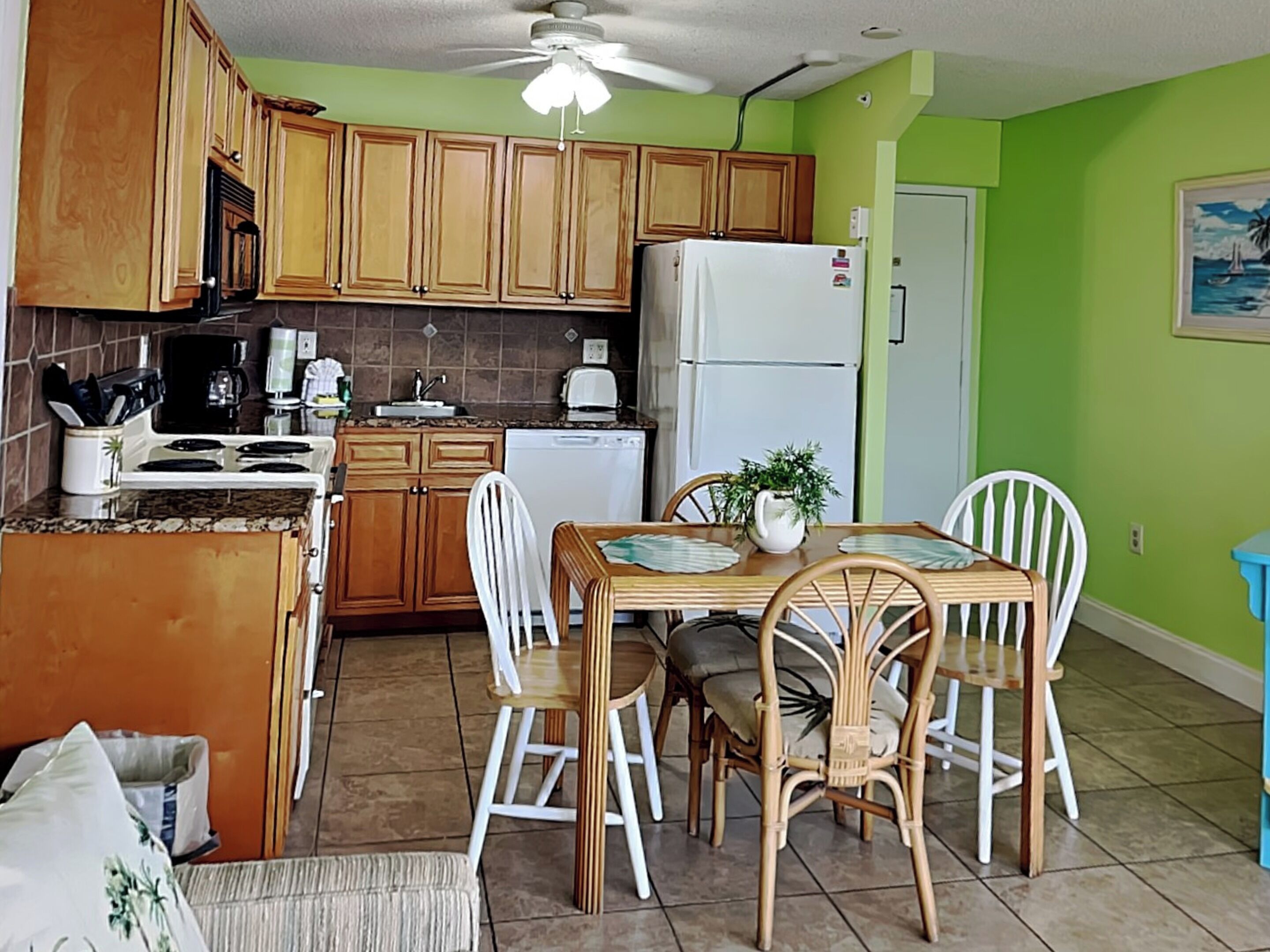 Una cocina compacta con armarios de madera, un refrigerador blanco y una mesa de comedor con sillas.