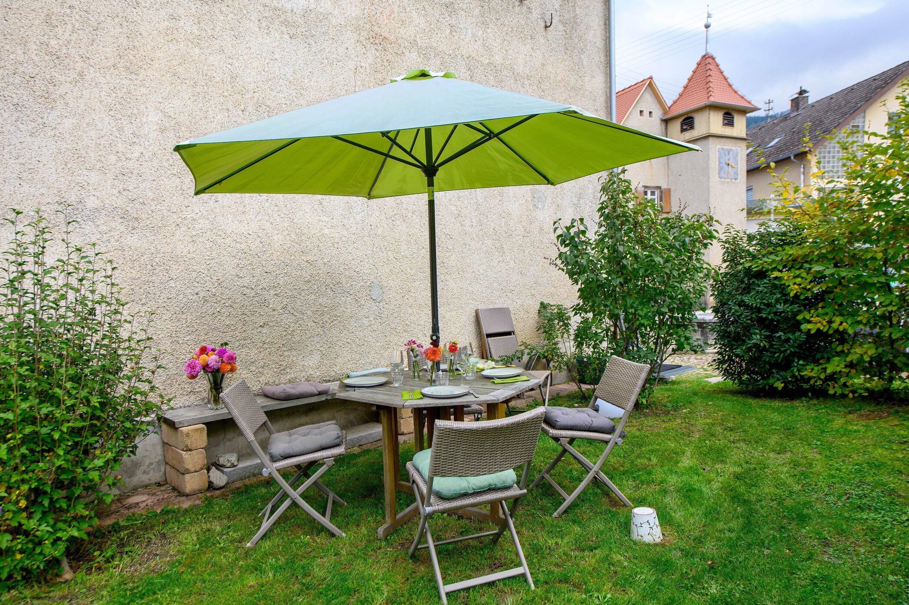 An outdoor dining area with a table, chairs, and a green umbrella.