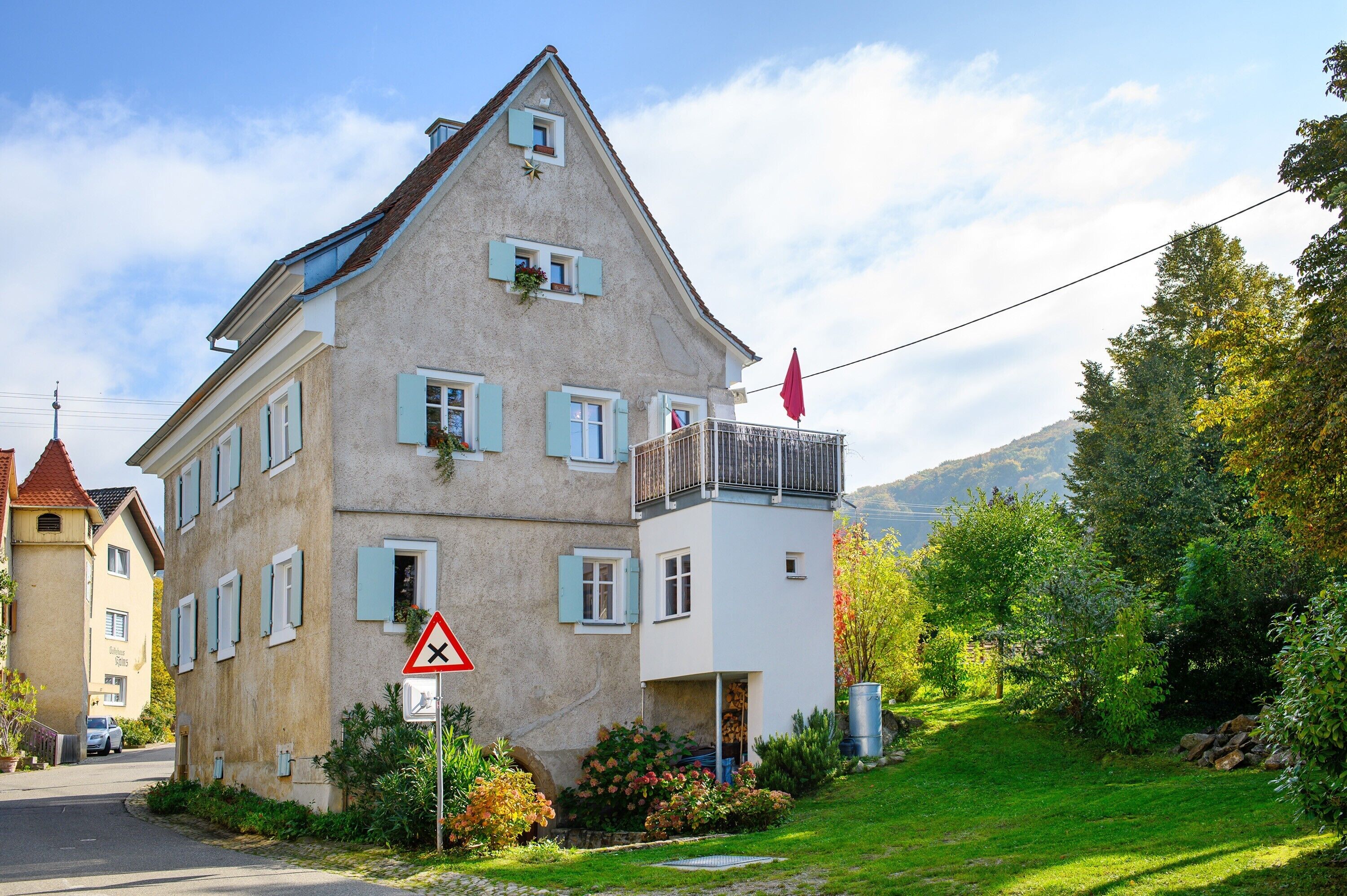 A two-story building with a balcony, a red flag, and a triangular warning sign.