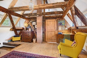 Una habitación rústica en el ático con vigas de madera a la vista, un escritorio de madera, un sillón amarillo y una alfombra roja estampada.