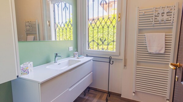 A bathroom with a white sink, a mirror, a window with a metal grill, and a towel rack with a towel.