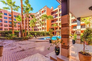 A hotel courtyard with a swimming pool, palm trees, and outdoor seating. - Top localisation, neuf, Piscine et une vue balcon (Marrakesh)