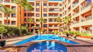 A hotel courtyard with a central swimming pool, multiple balconies, and surrounding palm trees. - Top localisation, neuf, Piscine et une vue balcon (Marrakesh)