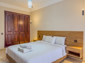 A bedroom with a wooden headboard, a large bed with white bedding, a nightstand, and a wooden wardrobe. - Top localisation, neuf, Piscine et une vue balcon (Marrakesh)