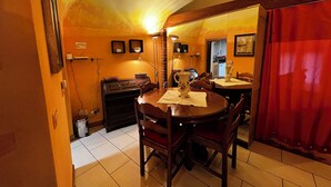Un coin repas avec une table ronde, des chaises, un vase et un rideau rouge.
