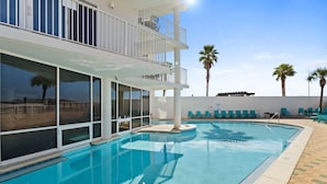 A swimming pool with a sunshade, lounge chairs, and a view of the beach.