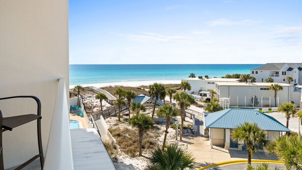 A beachfront hotel with a pool, palm trees, and a clear view of the ocean.
