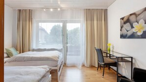 A room with two beds, a glass table, a chair, and a painting on the wall. - Room 'No. 5' with Shared Terrace, Shared Garden and Balcony (Dachsberg)