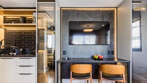 A modern kitchen with a built-in TV, two wooden chairs, and a fruit bowl on the counter. - GO Carlos Gomes by My Way (Porto Alegre)