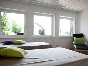Una habitación con dos camas, una silla y tres ventanas.