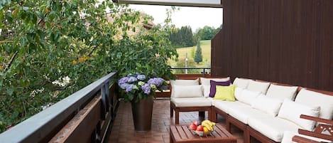 Een balkon met een houten bank, een bank en een tafel met fruit.