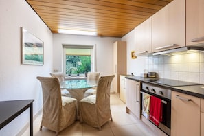 Une cuisine moderne avec une table à manger en verre, des chaises de couleur beige, une cuisinière et une fenêtre donnant sur un paysage verdoyant.