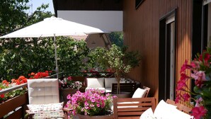 An outdoor seating area with wooden furniture, a large potted plant with pink flowers, and a white umbrella.