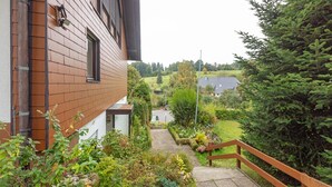 A residential building with a brick exterior, a wooden staircase, and a garden with various plants and a large evergreen tree.