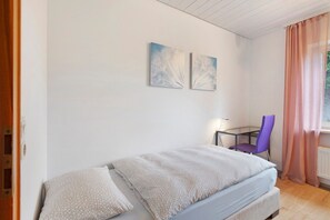 A single bed with a patterned blanket, a small table with a chair, and two wall-mounted artworks. - Room 'Single Room - No. 8 with Separate WC' with Shared Terrace and Shared Garden (Dachsberg)