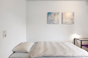 A bedroom with a bed, pillows, a nightstand, and two wall-mounted abstract paintings. - Room 'Single Room - No. 8 with Separate WC' with Shared Terrace and Shared Garden (Dachsberg)