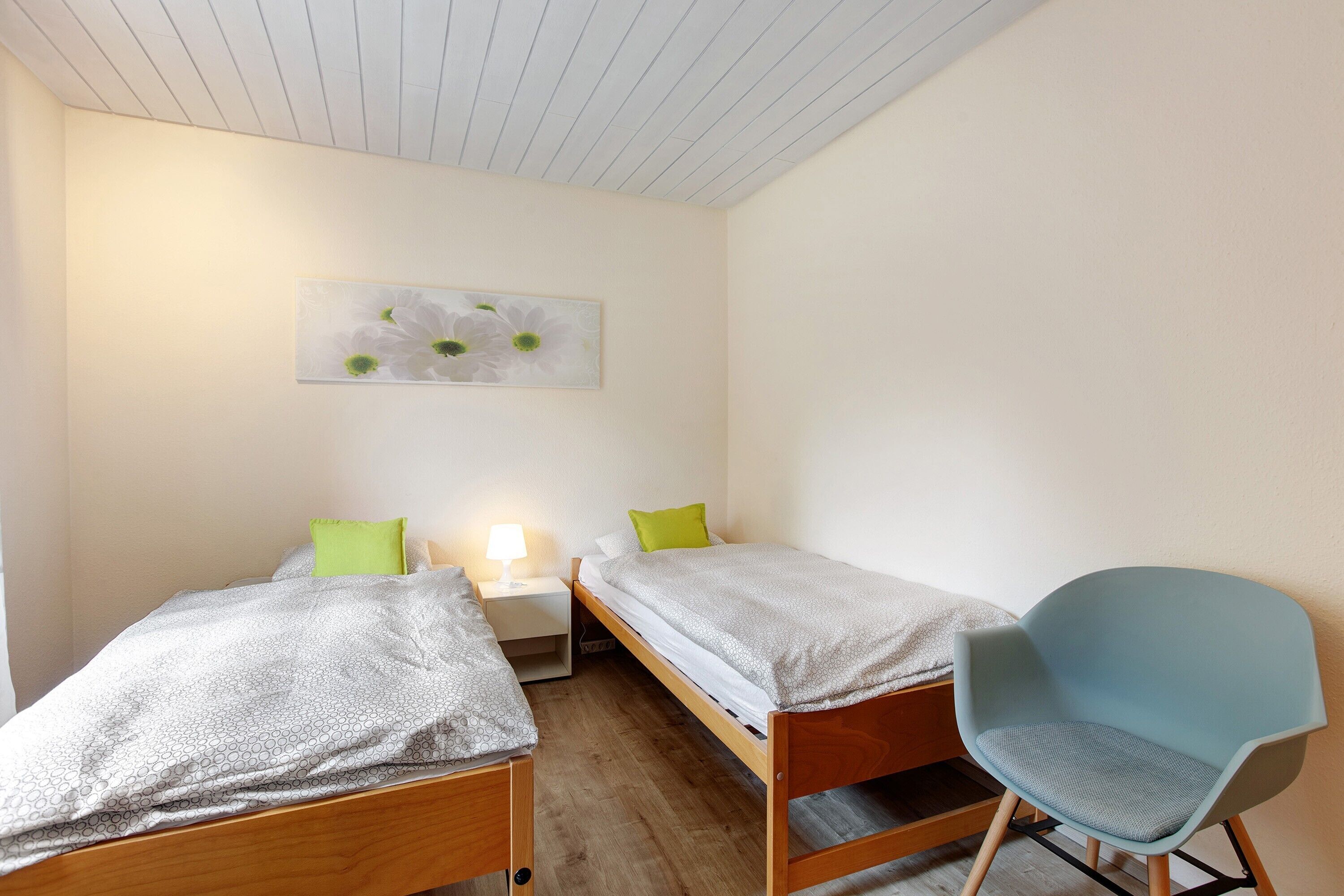 Un dormitorio con dos camas individuales, una mesita de noche, una silla y una lámpara fijada a la pared.