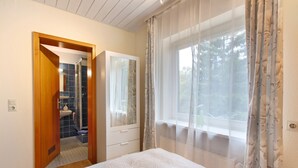 A bedroom with a bed, a window with curtains, a bathroom with a sink and mirror, and a wardrobe. - Room 'No. 7' with Shared Terrace and Shared Garden (Dachsberg)