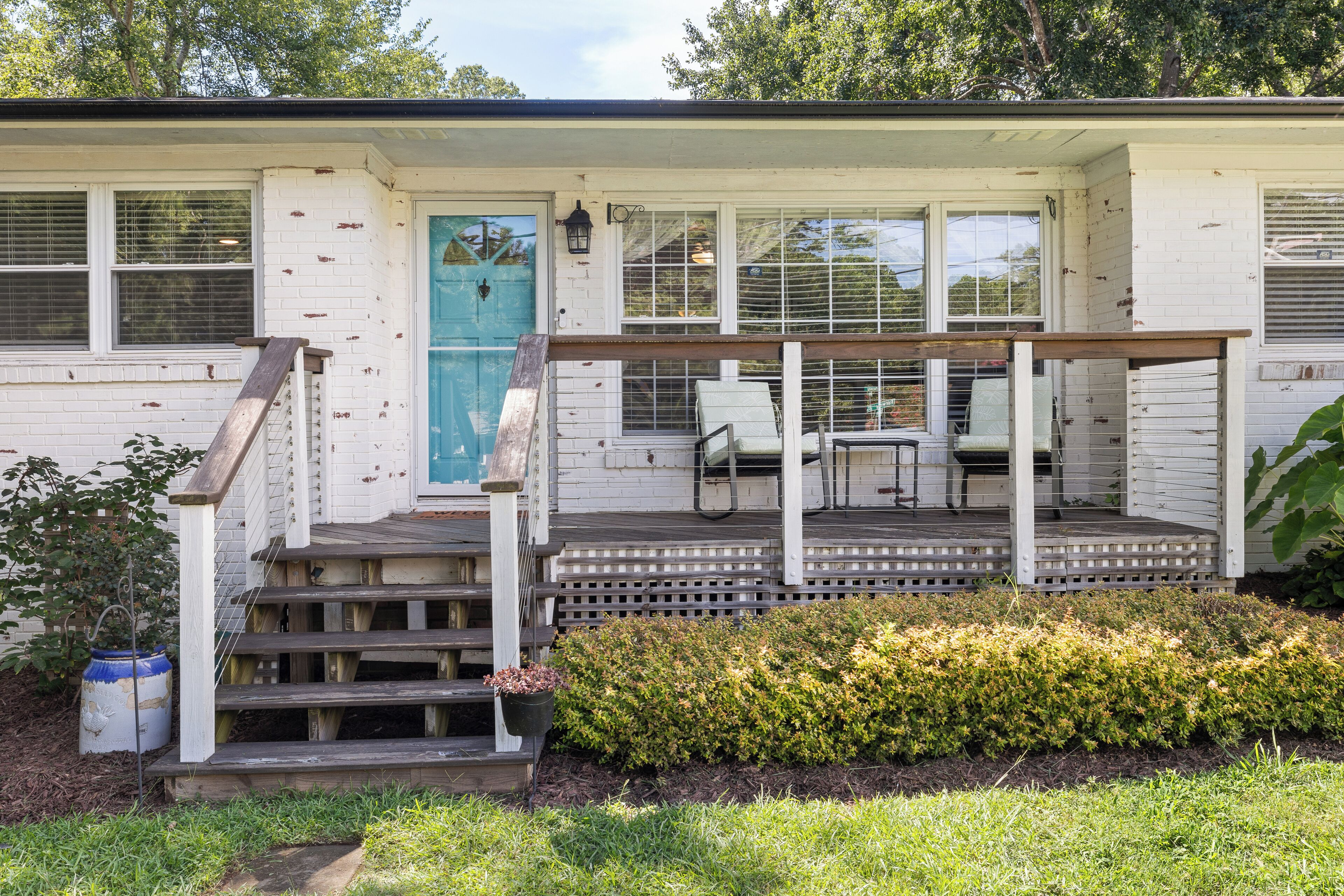A white house with a porch, a blue door, and a small garden area.
