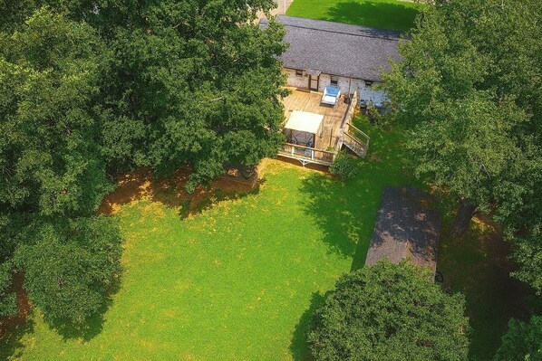 An aerial view of a property with a large grassy area, a building with a sloped roof, and a wooden deck.