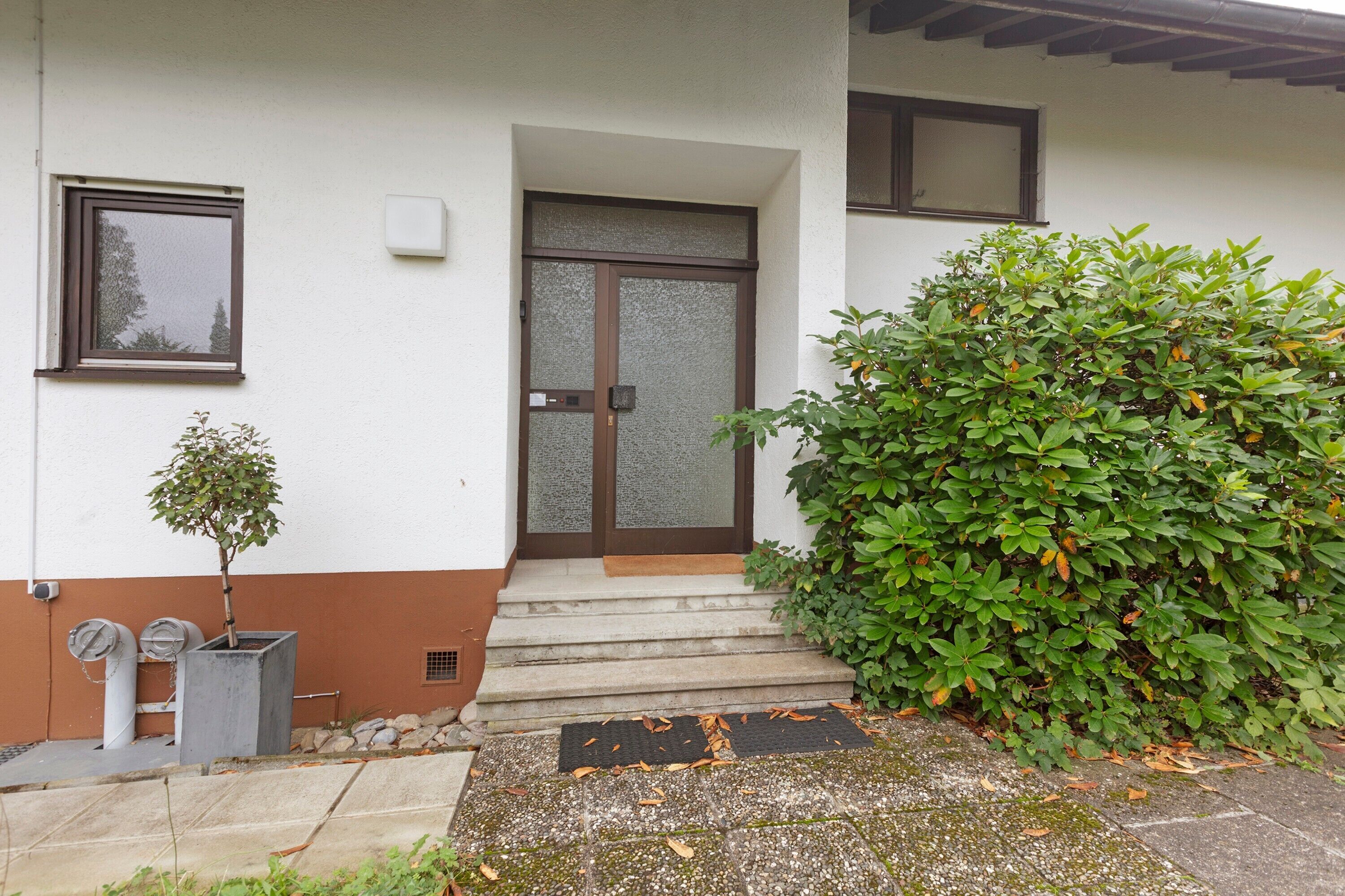 Une maison avec une porte d’entrée, des marches, un petit arbre et un arbuste.